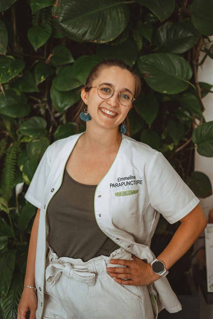 Emmeline, praticienne du réseau Parapuncture, en tenue de travail devant un mur végétal.