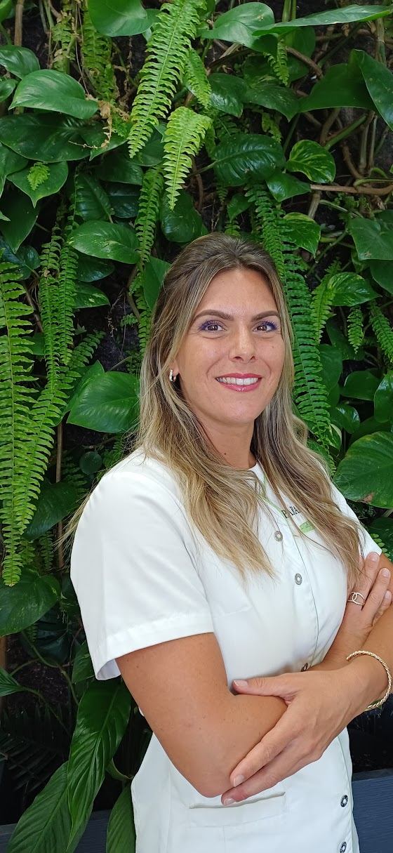 Justine, praticienne du réseau Parapuncture, en tenue de travail devant un mur végétal.